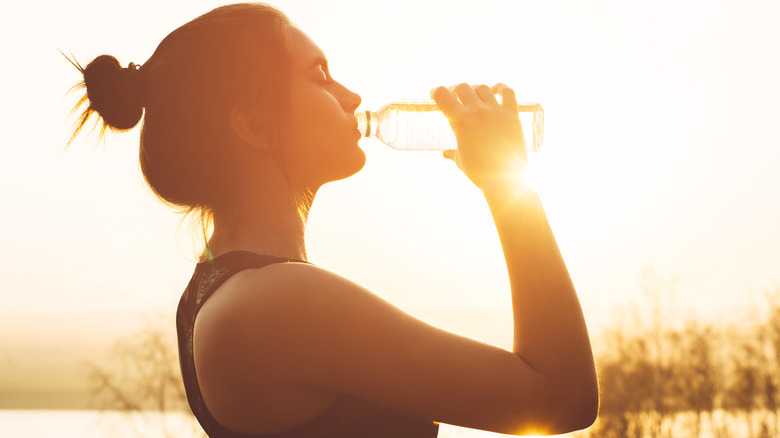 Woman drinking water from a bottle at sunset